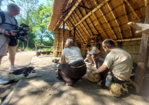 Cameraman filmt mensen in historische kledij aan een rieten hut in het vakantiepark Expedition Archeon.
