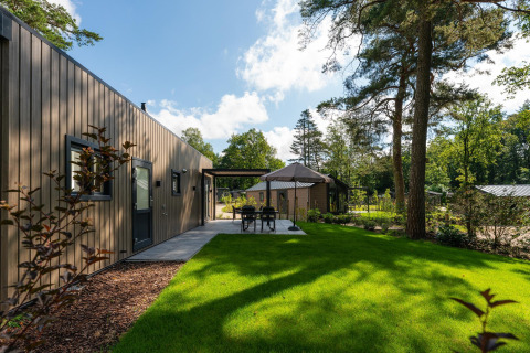 Loevestein Comfort lodge with wood exterior, green lawn, outdoor dining area and surrounding tall trees.