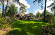 Moderne Loevestein Comfort-lodge i Veluwepark de Bosgraaf, Nederlandene, omgivet af grøn græsplæne og træer.