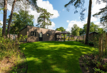 Lodge Loevestein Comfort en Veluwepark de Bosgraaf, Países Bajos, rodeado de césped verde y árboles altos.