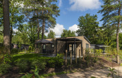 Udendørsfoto af Loevestein Comfort-lodge i Veluwepark de Bosgraaf, omgivet af grønne træer og natur.