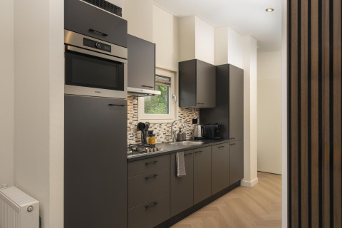 Modern kitchenette with dark cabinets, built-in appliances, and window at Loevestein Comfort, Veluwepark de Bosgraaf, Netherlands.