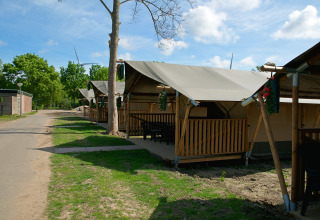 Safaritent met toilet bij Camping de Krabbeplaat in Nederland, omringd door bomen en een pad.