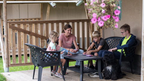 Gezin met kinderen en hond speelt kaartspel op terras van safaritent bij Camping de Krabbeplaat.