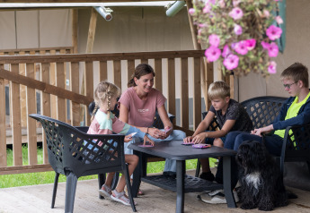 Familie mit Kindern und Hund spielt Karten auf der Terrasse eines Safarizelts auf Camping de Krabbeplaat.