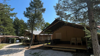 Tienda safari con baño y terraza de madera en zona boscosa, cielo soleado y despejado.