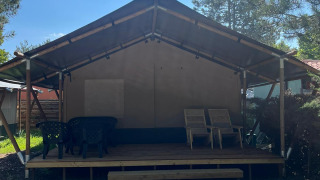 Safaritent met veranda en tuinmeubilair bij Camping Luna del Monte in Italië, omgeven door bomen.