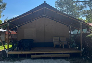 Safari-Zelt mit Veranda und Gartenmöbeln auf dem Campingplatz Luna del Monte, umgeben von Bäumen.