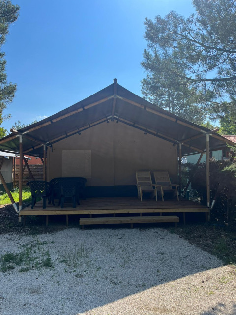 Safari tent with a veranda and outdoor seating at Camping Luna del Monte in Italy, surrounded by trees.
