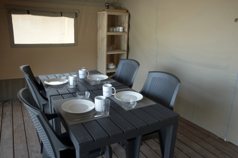 Zona pranzo in tenda safari con quattro coperti e scaffale in legno al Camping Luna del Monte, Italia.