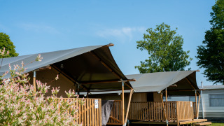 Safaritenten met eigen sanitair op Camping Tussen de Diepen in Nederland onder een heldere, blauwe lucht.