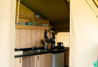 Blick in das Küchenbereich eines Safarizelts mit Holzmöbeln bei Camping Tussen de Diepen in den Niederlanden.