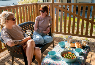 Deux femmes dégustent un repas et du vin sur la terrasse d'une tente safari au Camping Tussen de Diepen.