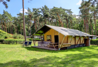 Tente safari avec terrasse et coin salon, entourée d’arbres, à Familiepark Goolderheide en Belgique.