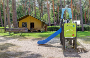 Tienda safari con baños privados y un tobogán en Familiepark Goolderheide, Bélgica, rodeada de árboles.