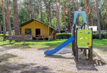 Tienda safari con baños privados y un tobogán en Familiepark Goolderheide, Bélgica, rodeada de árboles.