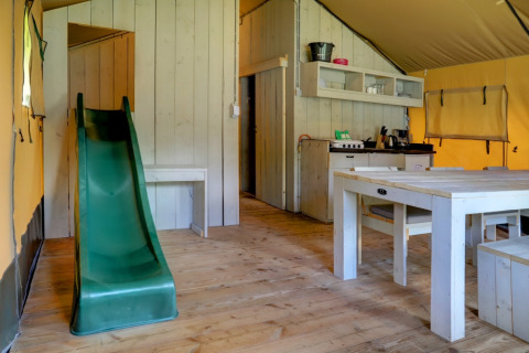 Interior de tienda safari con tobogán, mesa de comedor y cocina en Familiepark Goolderheide, Bélgica.