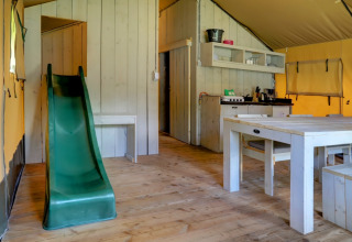 Interior of safari tent featuring a green slide, rustic dining table and kitchenette at Familiepark Goolderheide, Belgium.