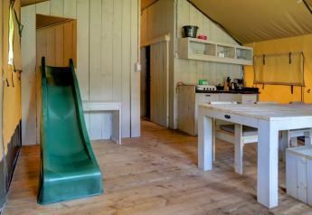 Interior de tienda safari con tobogán, mesa de comedor y cocina en Familiepark Goolderheide, Bélgica.