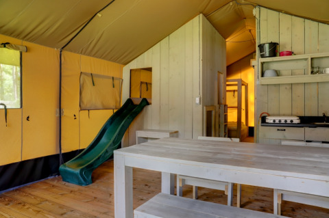 Interieur van een safaritent met houten tafel, glijbaan, keuken en stapelbed bij Familiepark Goolderheide.