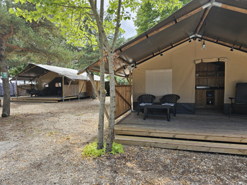 Tenda safari con veranda privata e servizi igienici, circondata da alberi, perfetta per il glamping.