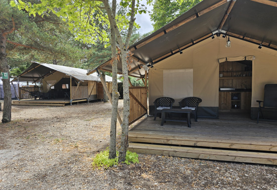 Tenda safari con veranda privata e servizi igienici, circondata da alberi, perfetta per il glamping.