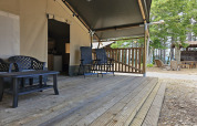 Terraza de madera con asientos delante de una tienda safari con instalaciones sanitarias en Camping Luna del Monte, Italia.
