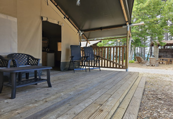 Terraza de madera con asientos delante de una tienda safari con instalaciones sanitarias en Camping Luna del Monte, Italia.