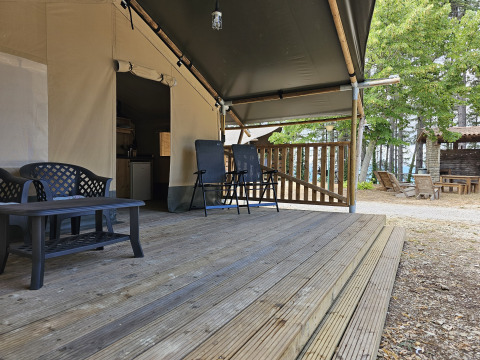 Wooden deck with seating in front of a safari tent with sanitary facilities at Camping Luna del Monte in Italy.