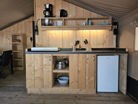 Küchenbereich im Safarizelt mit Holzmöbeln, Kühlschrank und Regalen auf Camping Luna del Monte, Italien.