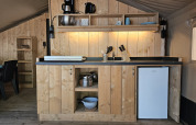 Kitchen area inside a safari tent with wooden cabinets, fridge, and appliances at Camping Luna del Monte, Italy.