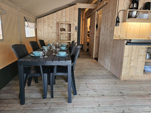 Binnenkant van safaritent met eettafel, keuken en sanitaire voorzieningen op Camping Luna del Monte in Italië.