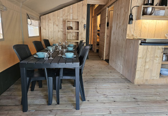Interior de tienda safari con mesa de comedor, cocina y sanitarios en Camping Luna del Monte, Italia.