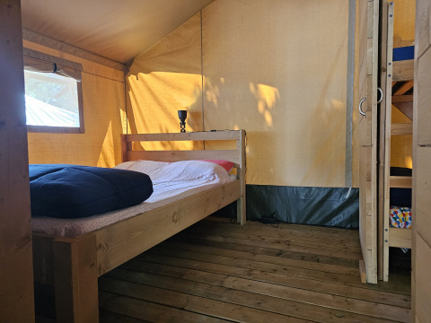 Vista interna di una tenda safari con pavimento in legno, letto matrimoniale e letto a castello al Camping Luna del Monte in Italia.