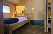Interior view of a safari tent with wooden floor, double bed, and bunk bed at Camping Luna del Monte in Italy.