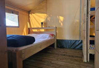 Vista interna di una tenda safari con pavimento in legno, letto matrimoniale e letto a castello al Camping Luna del Monte in Italia.