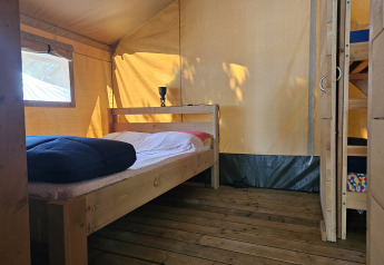 Interior view of a safari tent with wooden floor, double bed, and bunk bed at Camping Luna del Monte in Italy.