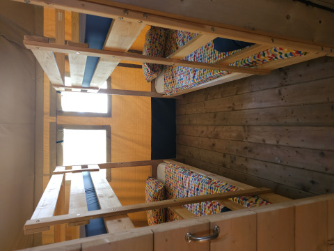 Vier Einzelbetten in Etagenbetten im Safarizelt mit Holzboden und bunten Bettbezügen auf Camping Luna del Monte.