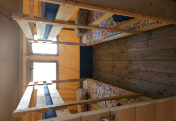 Four single beds in bunk style with colorful bedding inside a safari tent at Camping Luna del Monte, Italy.