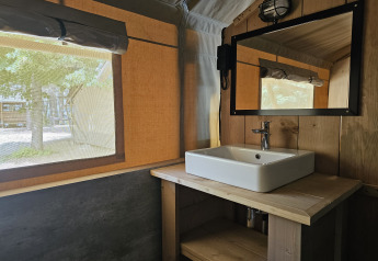 Interno di tenda safari con bagno privato al Camping Luna del Monte, Italia, con lavandino e specchio.