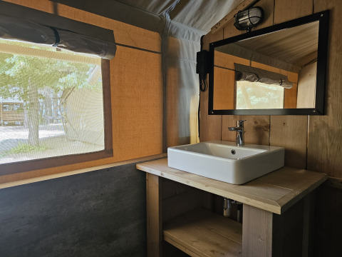 Interno di tenda safari con bagno privato al Camping Luna del Monte, Italia, con lavandino e specchio.