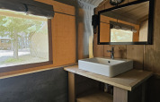 Interior de tienda safari con baño privado en Camping Luna del Monte, Italia, con lavabo y espejo.