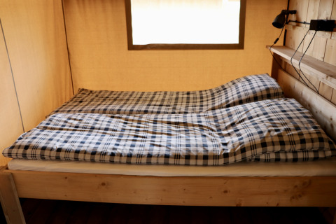 Interieur van een safaritent met tweepersoonsbed en geruite dekens bij Camping de Heerlijkheid Vorenseinde.