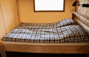Interior de una tienda safari con cama doble y ropa de cama a cuadros en Camping de Heerlijkheid Vorenseinde.