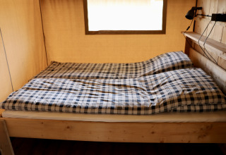 Interior de una tienda safari con cama doble y ropa de cama a cuadros en Camping de Heerlijkheid Vorenseinde.