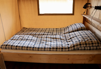 Interior de una tienda safari con cama doble y ropa de cama a cuadros en Camping de Heerlijkheid Vorenseinde.