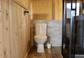 Bathroom with wooden panels, toilet, and shower in a safari tent at Camping de Heerlijkheid Vorenseinde.