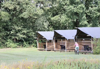 Safari tents with porches and a cyclist in front at Camping de Heerlijkheid Vorenseinde in the Netherlands.