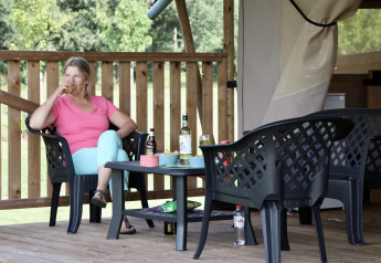 Donna beve seduta a un tavolo davanti a una tenda safari con servizi igienici a Camping de Heerlijkheid Vorenseinde.
