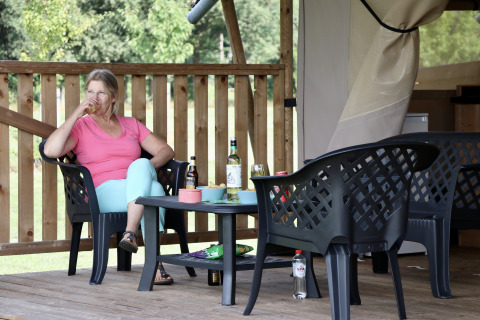 Vrouw drinkt aan een tafel bij een safaritent met sanitair op Camping de Heerlijkheid Vorenseinde.